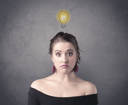 A teen student girl with funny facial expression has a good idea illustrated by a drawn light bulb lighting up above the head on the grey wall background concept.