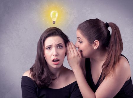 A young girl has an idea illustrated with a drawn glowing light bulb above the head, while a friend whispers a secret in her ear concept.