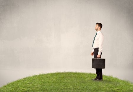 A successful caucasian elegant business man standing in small green grass with briefcase in front of clear empty background concept.