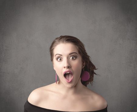 pretty-young-teenage-girl-standing-front-630807350 A pretty young teenage girl standing in front of a grey clear empty urban wall background concept while making funny faces.