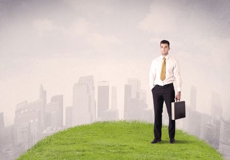 A confident male well looking office manager standing in small green grass in front of city landscape with tall buildings concept.