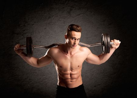 A handsome fitness guy lifting weight and showing his strong muscles in front of a black urban concrete wall concept