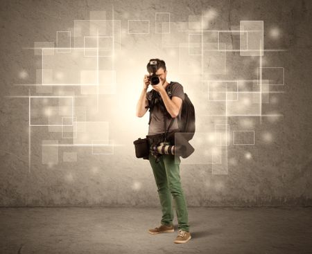 A hobby photographer with professional camera gear and belt shooting in front of brown sepia urban concrete wall full of glowing square illustrations concept