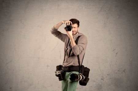 A professional male photographer with belt holding a camera and taking photos in front of clear grey urban wall background concept