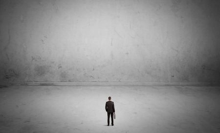 A tiny elegant businessman standing in large empty urban space with concrete walls and grey background concept