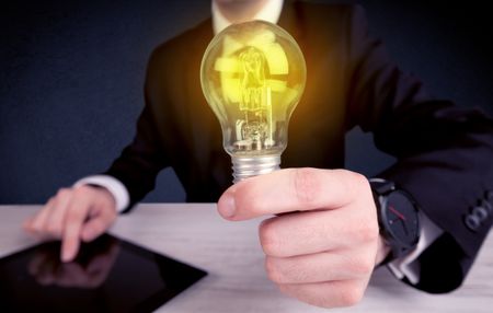 A business man in suit holding a glowing yellow light bulb in his hand while working in the office concept.
