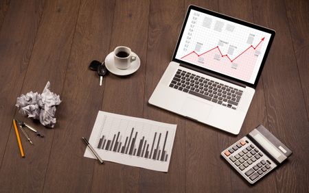 Computer wooden desk with laptop and red arrow chart in screen