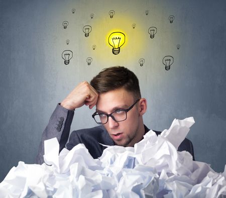 Young businessman sitting behind crumpled paper with lightbulbs above his head