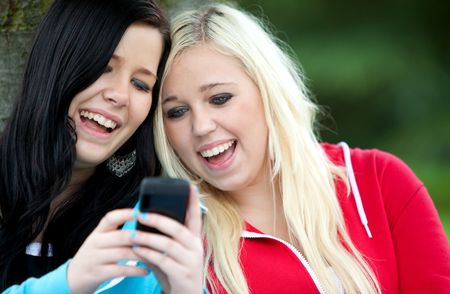 Happy women friends texting on a cell phone  outdoors