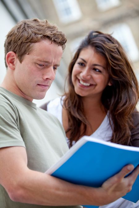 Happy couple of students with a notebook and smiling outdoors