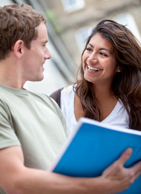 Happy couple of students with a notebook and smiling outdoors