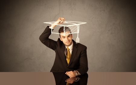 An elegant, successful university student drawing himself a square academic mortarboard cap with a chalk in front of grey wall background concept