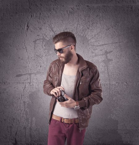 A hipster fashion model guy in casual clothing stnading with mobile phone in front of concrete urban wall background concept