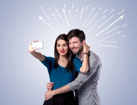 A cheerful young couple taking selfie photo with mobile phone and white lines and arrows pointing to the sky above them concept