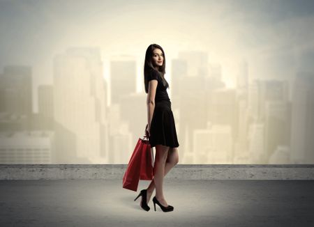 Attractive lady in black holding red shopping bags standing in front o urban landscape with tall buildings concept