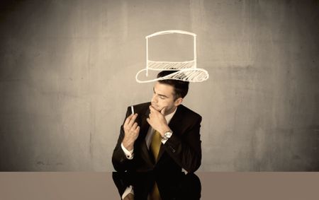 A young happy businessman in elegant suit drawing funny hat and mustache in empty grey space with a chalk illustration concept