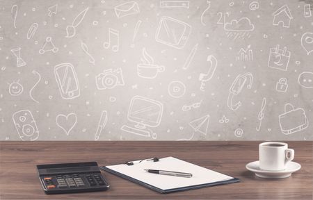 Close up of business office desk with laptop tablet in front of brown wall background full of drawn communication icons and school items concept