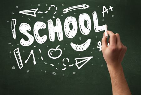 A teacher writing school, drawing children things on clean green chalkboard by hand