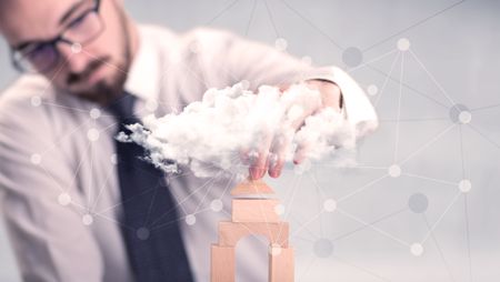 Young handsome businessman using wooden building blocks behind cloud concept 