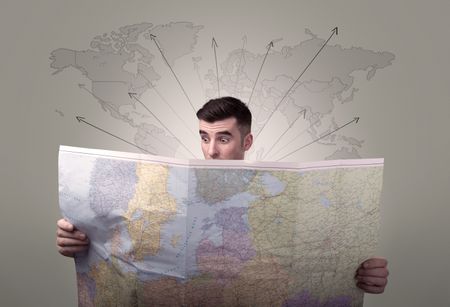 Handsome young man holding a map with world map and arrows behind him