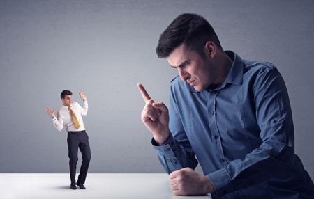 Young professional businessman being angry with an other miniature businessman in front of a grey background