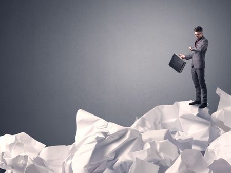 Thoughtful young businessman standing on a pile of crumpled paper with a grey background