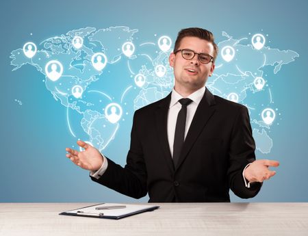 Young handsome businessman sitting at a desk with a blue world map behind him