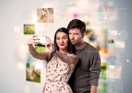 Collecting memories concept with photos in backbround and a happy young couple in love taking selfie with a mobile phone