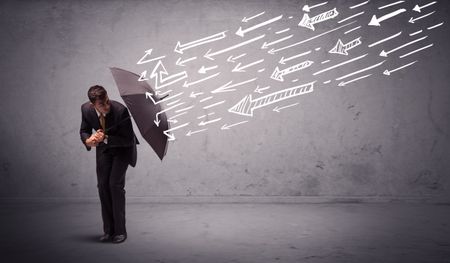 Business man standing with umbrella and drawn arrows hitting him on grungy background