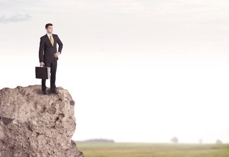 A successful good looking business person standing on top of a high cliff above country landscape with clear white sky concept