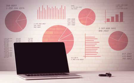 A professional laptop with blank screen sitting on a white office desk in front of wall full of pie charts and graphs concept