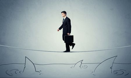 A brave businessman walking on tightrope expanded aboved rawn ocean with shark fin concept