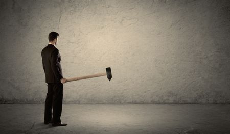 Business man standing in front of a grungy copyspace wall with a hammer