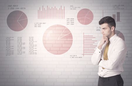 Young sales business male in elegant suit standing in front of brick wall background with lines and pie charts concept