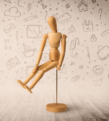 Wooden mannequin posed in front of a greyish background with mixed media scribbles behind it