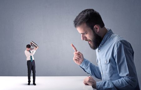 Young professional businessman being angry with an other miniature businessman in front of a blueish grey background