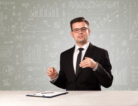 Young handsome businessman sitting at a desk with white graphs and calculations behind him 