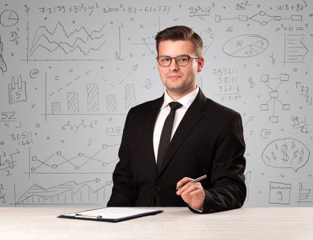 Young handsome businessman sitting at a desk with white charts behind him