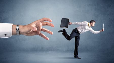 Young miniature businessman running from a big hand 