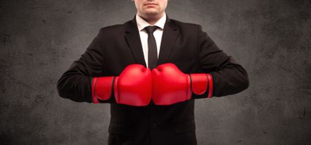 well-dressed-sales-person-standing-red-636058829 A well dressed sales person standing with red boxing gloves on his hand in front of urban grey wall background concept.