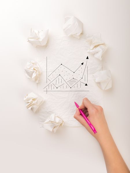 Female hand next to a few crumpled paper balls drawing a progress chart