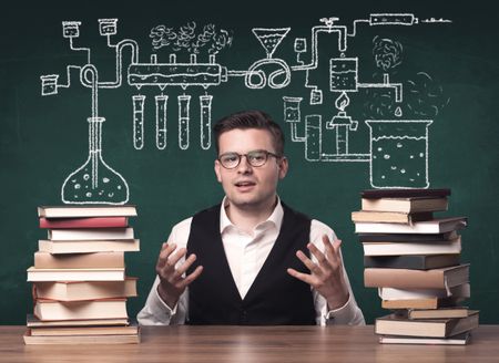 A young chemistry teacher in the middle of a chemical process explanation with tubes, reactions drawn on the blackboard back to school concept.