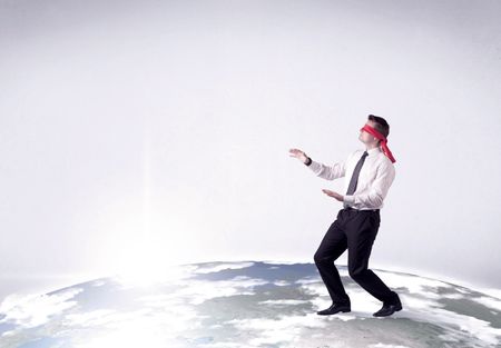 Young blindfolded businessman steps on a realistic globe