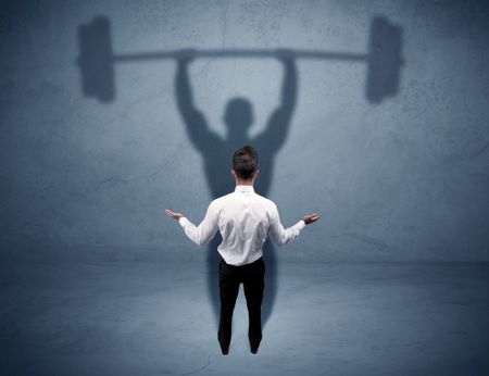 A confident young elegant salesman with briefcase facing a wall, looking at his strong, weight lifting shadow concept