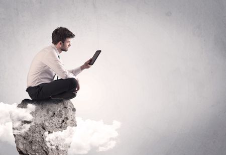 An elegant  smart businessman with laptop sitting in empty grey space on top of a cliff, between clouds concept
