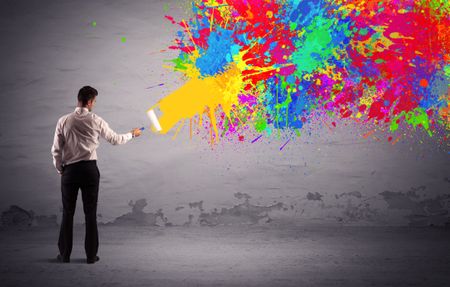 An elegant businessman in suit painting colorful splatter, bright colors on grey urban wall with a paint roller in his hand concept
