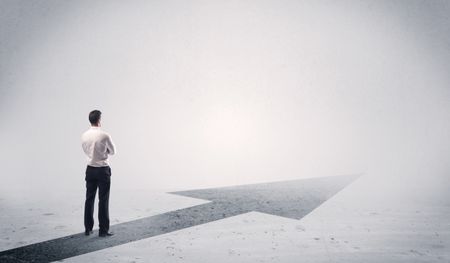 A professional businessman thinking while standing on a black arrow pointing forward in grey space concept