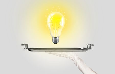 Serving a bright business idea concept using a bulb with bright sparkling warm yellow light presented on a silver plate