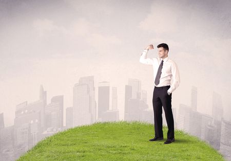 A confident male well looking office manager standing in small green grass in front of city landscape with tall buildings concept.