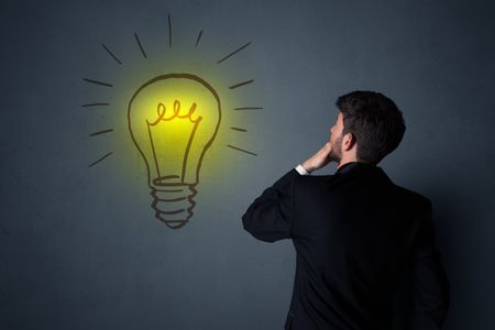 Young businessman in black suit standing in front of a drawn yellow lightbulb 